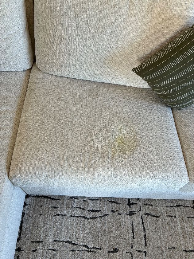 Food-related yellow stain on a light-colored couch cushion before upholstery cleaning in Clairemont