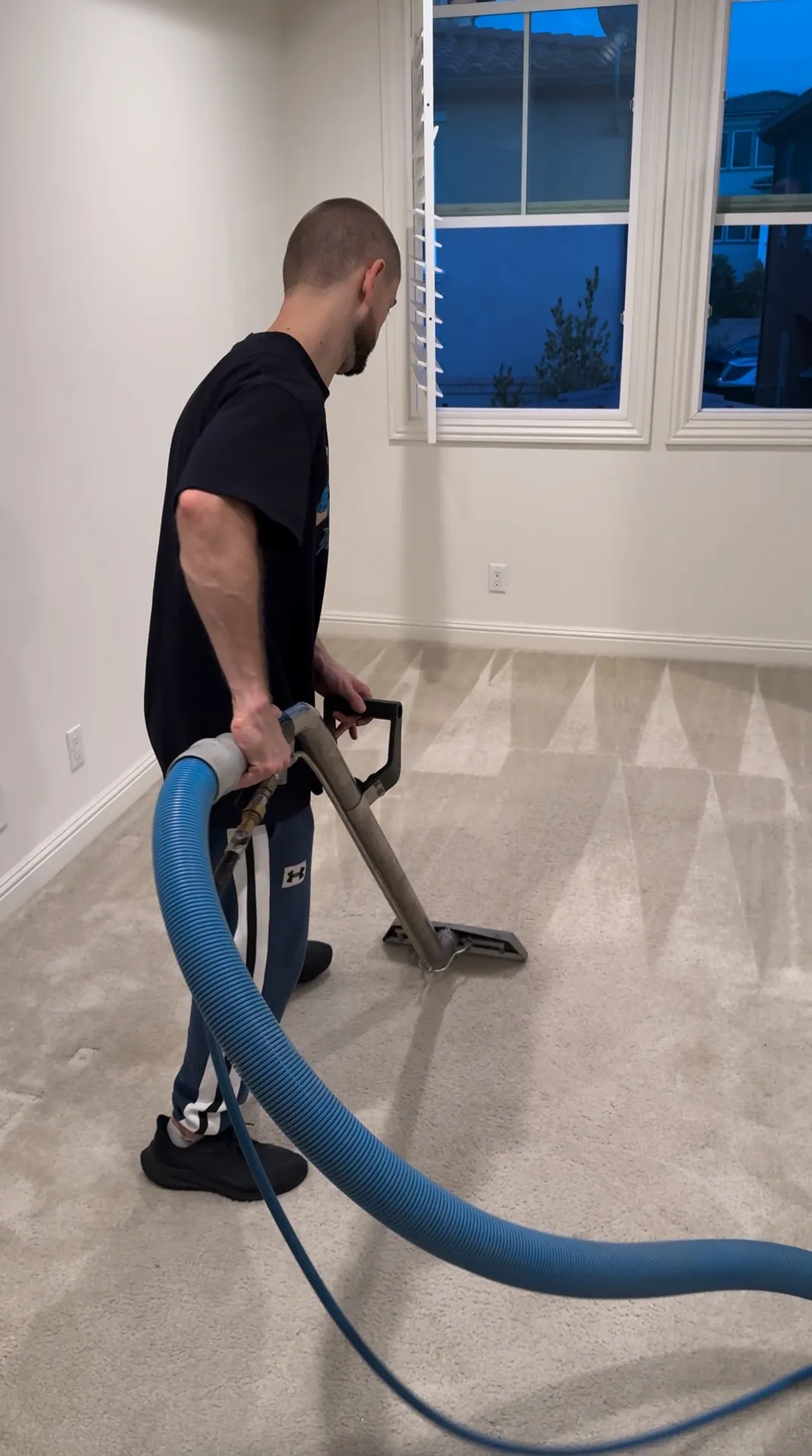 Mango Spotless technician performing carpet cleaning with a hot water extraction wand and hose in Del Mar, CA.