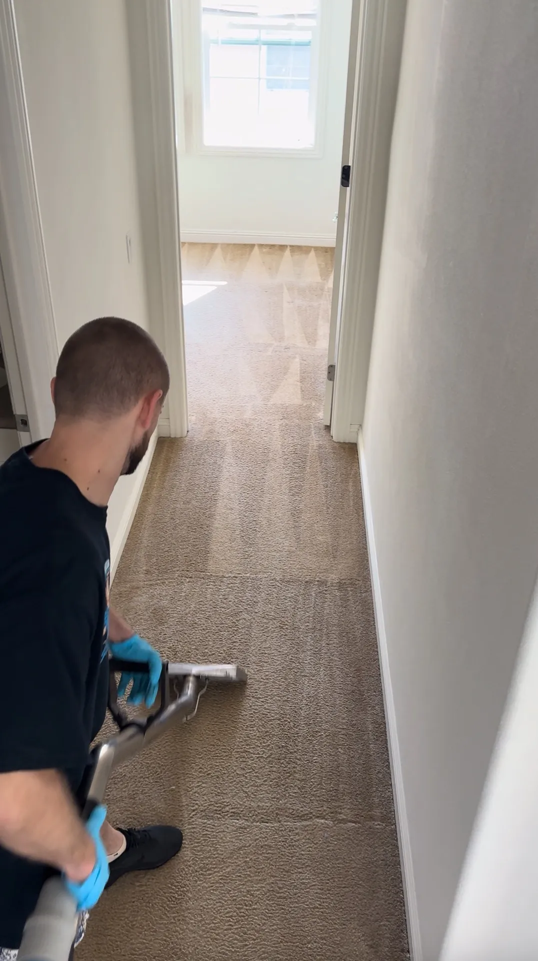 Technician cleaning a carpeted hallway with a carpet cleaning wand.