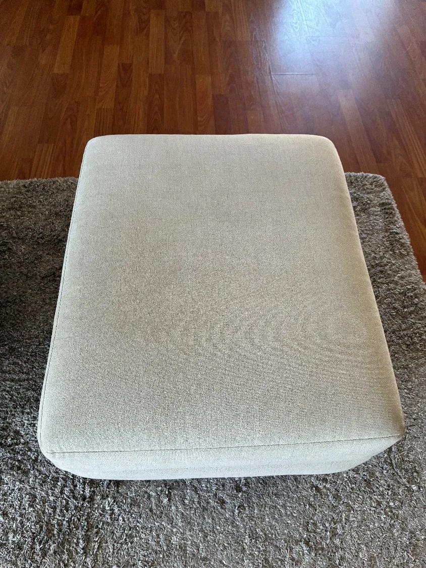 The matching ottoman cushion after cleaning, resting on the area rug